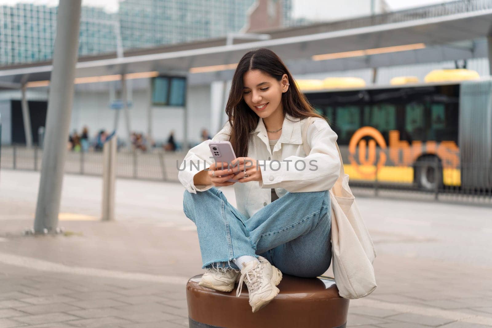 Caught in the moment, a young woman checks her bus itinerary, blending urban life and digital connection at a bustling bus stop.