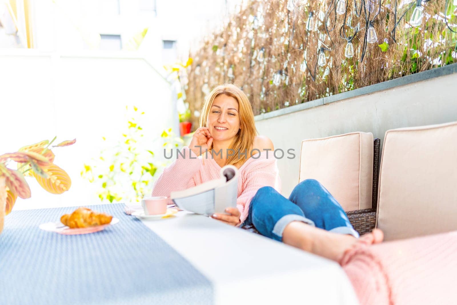 Cute woman reading a book sitting comfortable in the courtyard under an umbrella in a sunny day