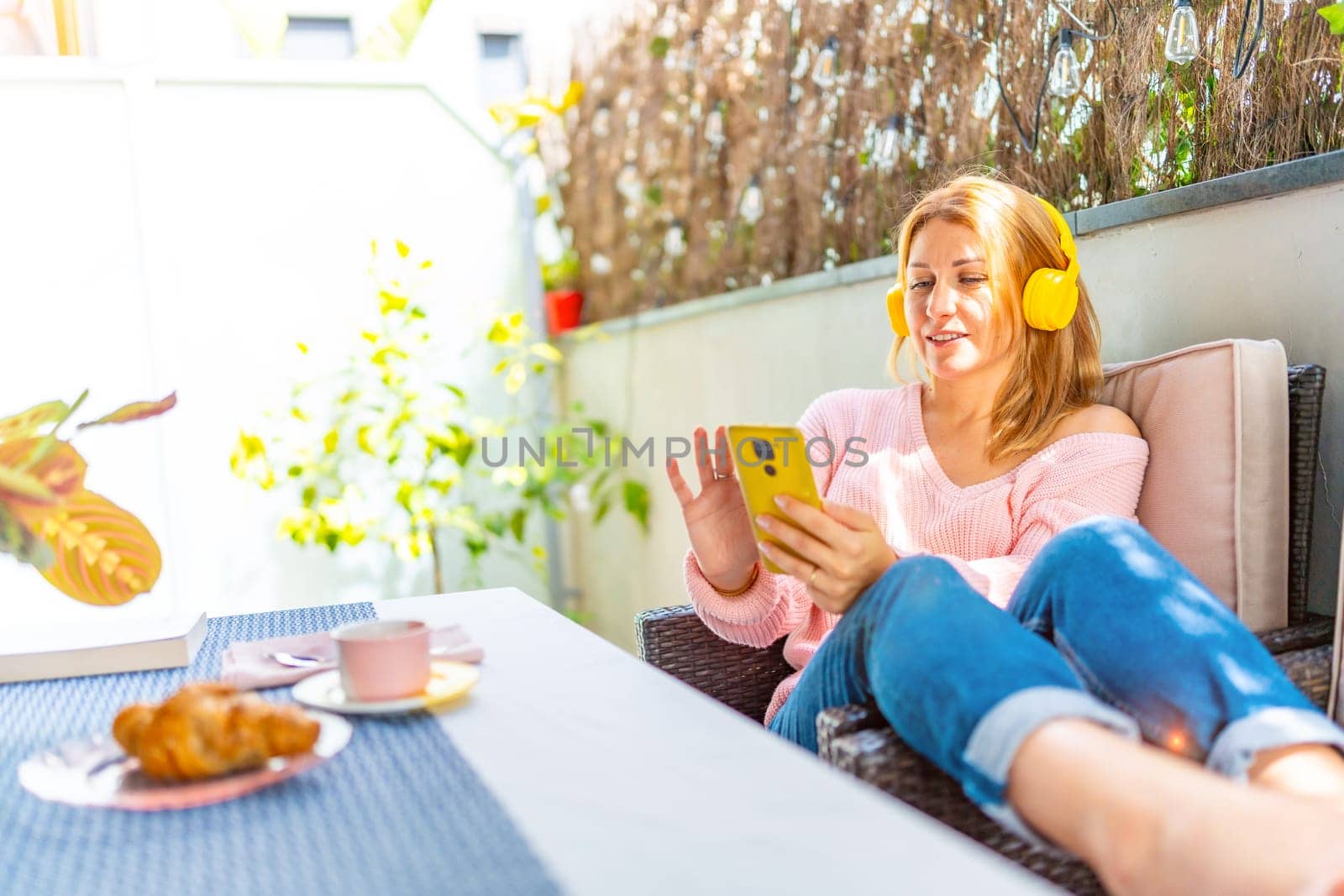 Caucasian adult, woman relaxing at the patio using smart phone and listening to music in the morning