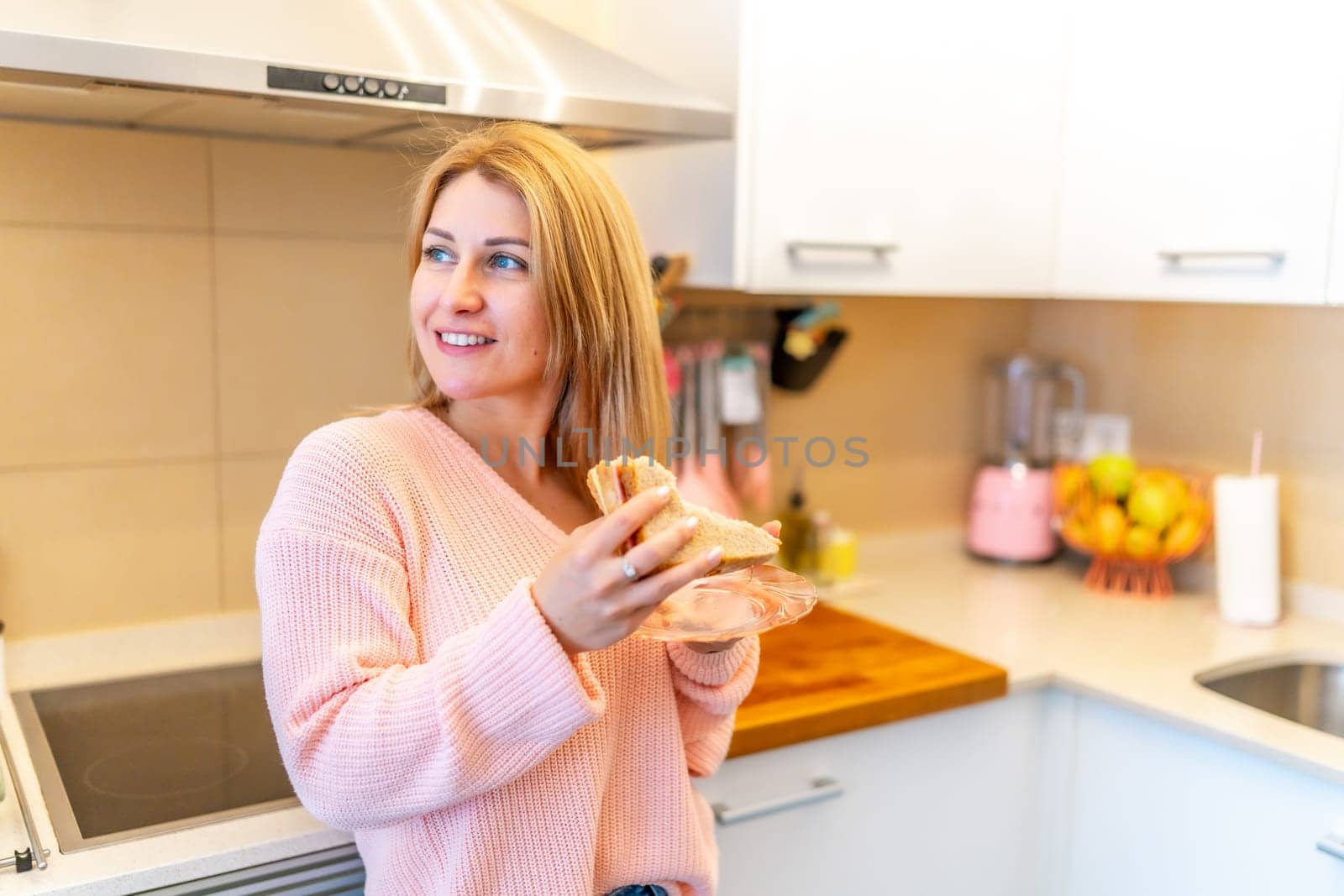 Caucasian blonde woman enjoying fresh made healthy sandwich standing on the kitchen