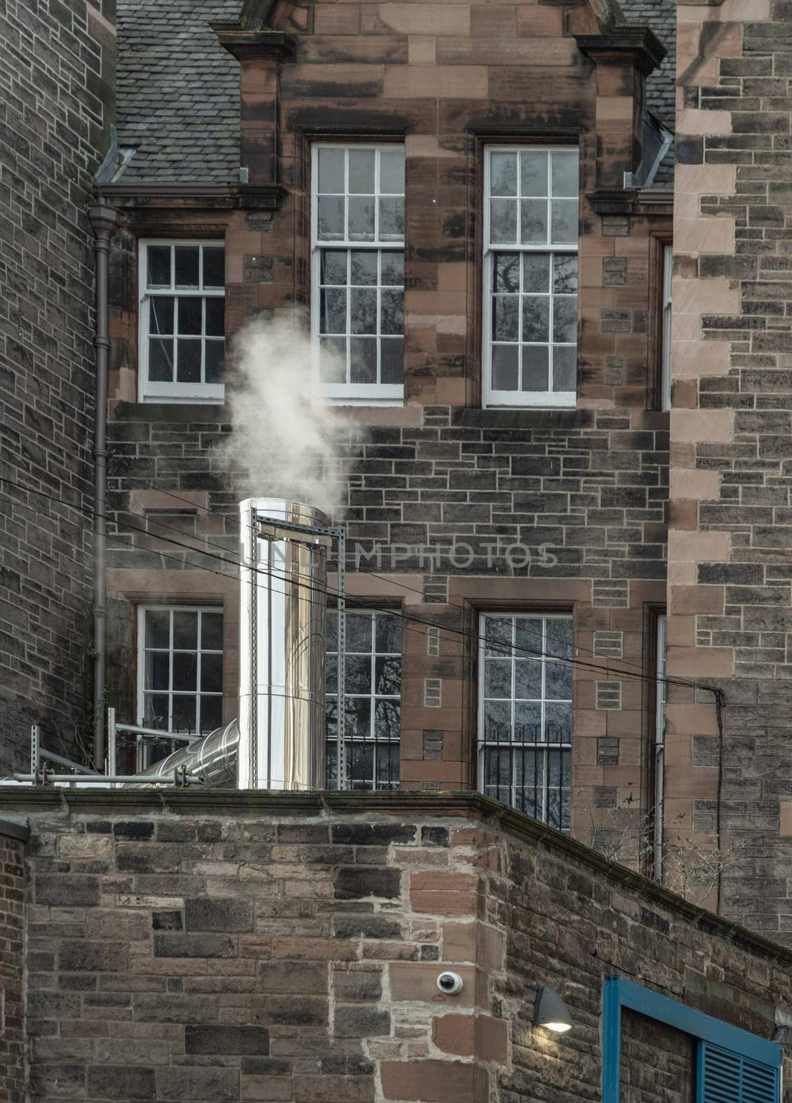 Edinburgh, Scotland - Jan 19, 2024 - Smoke from a Steel Chimney of Medieval Scottish Building in Edinburgh, Scotland. Brick wall of Old building, Space for text, Selective focus.