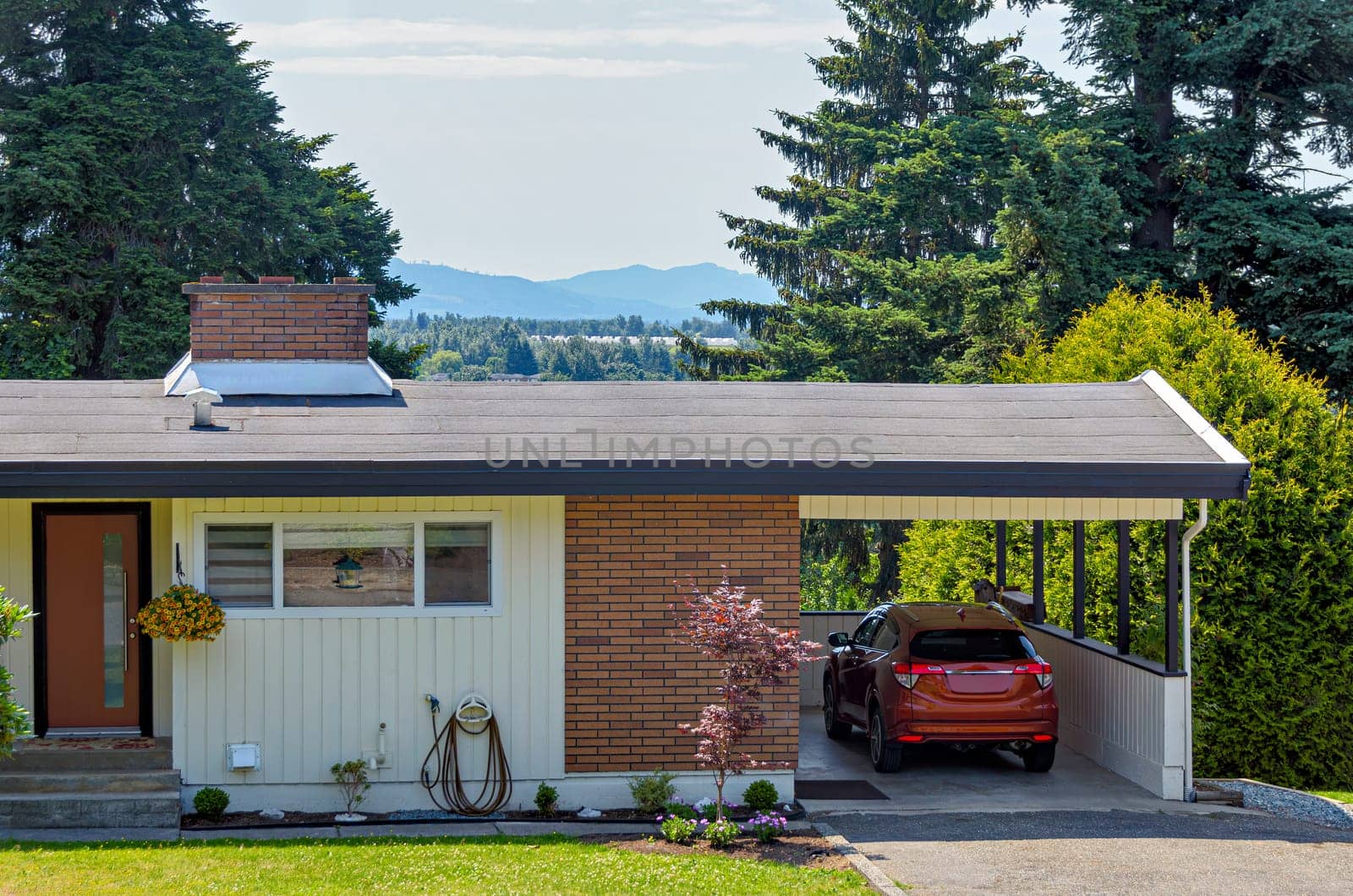 Average family house with mountain view and red car parked under the carport.