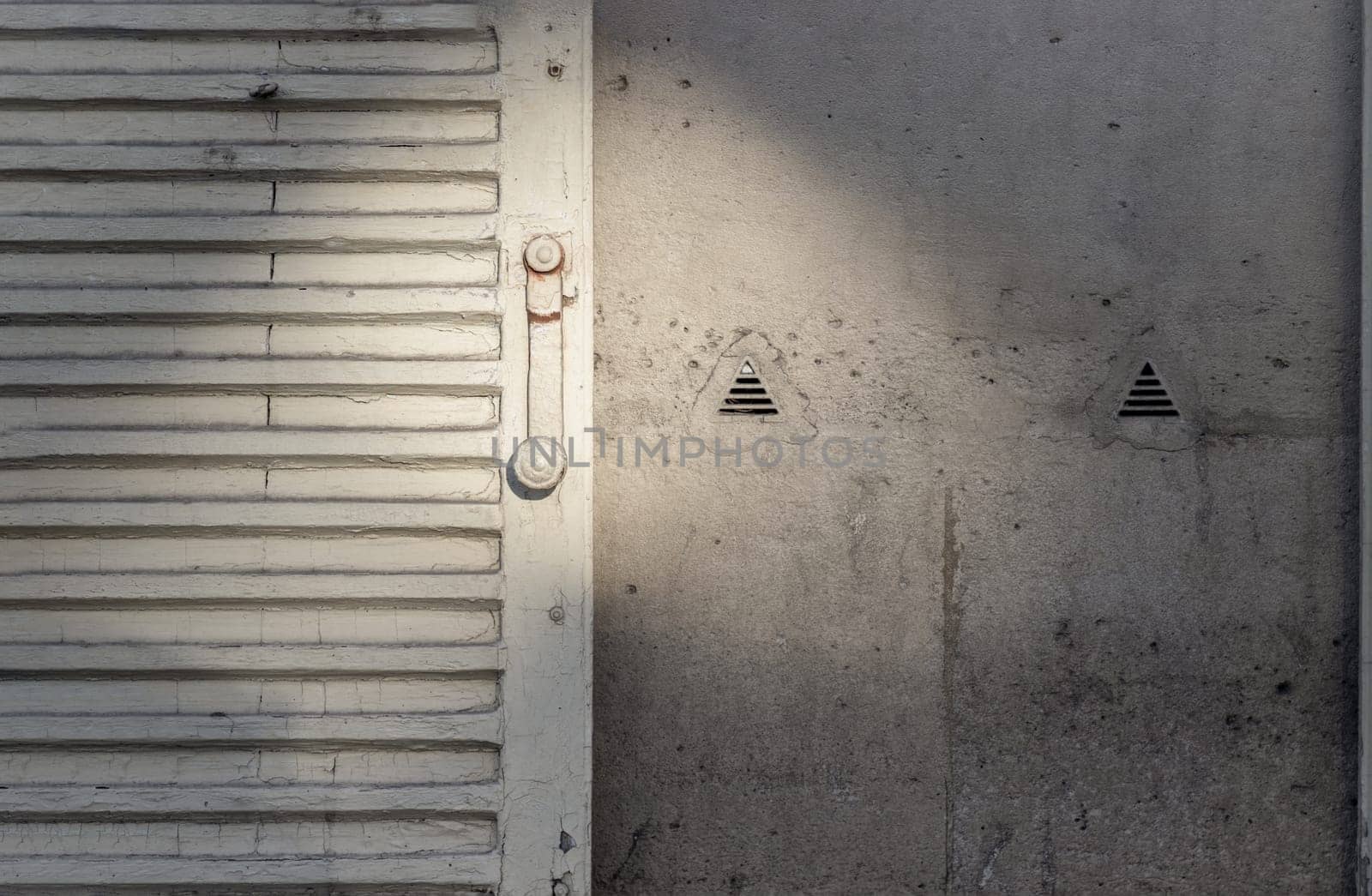 France, Paris - Jan 03, 2024 - The sun is shining through Vintage French Louvred Shutters and Two Knapen Siphons on wall (to vent damp air from inside the wall). Copy space, Selective focus.