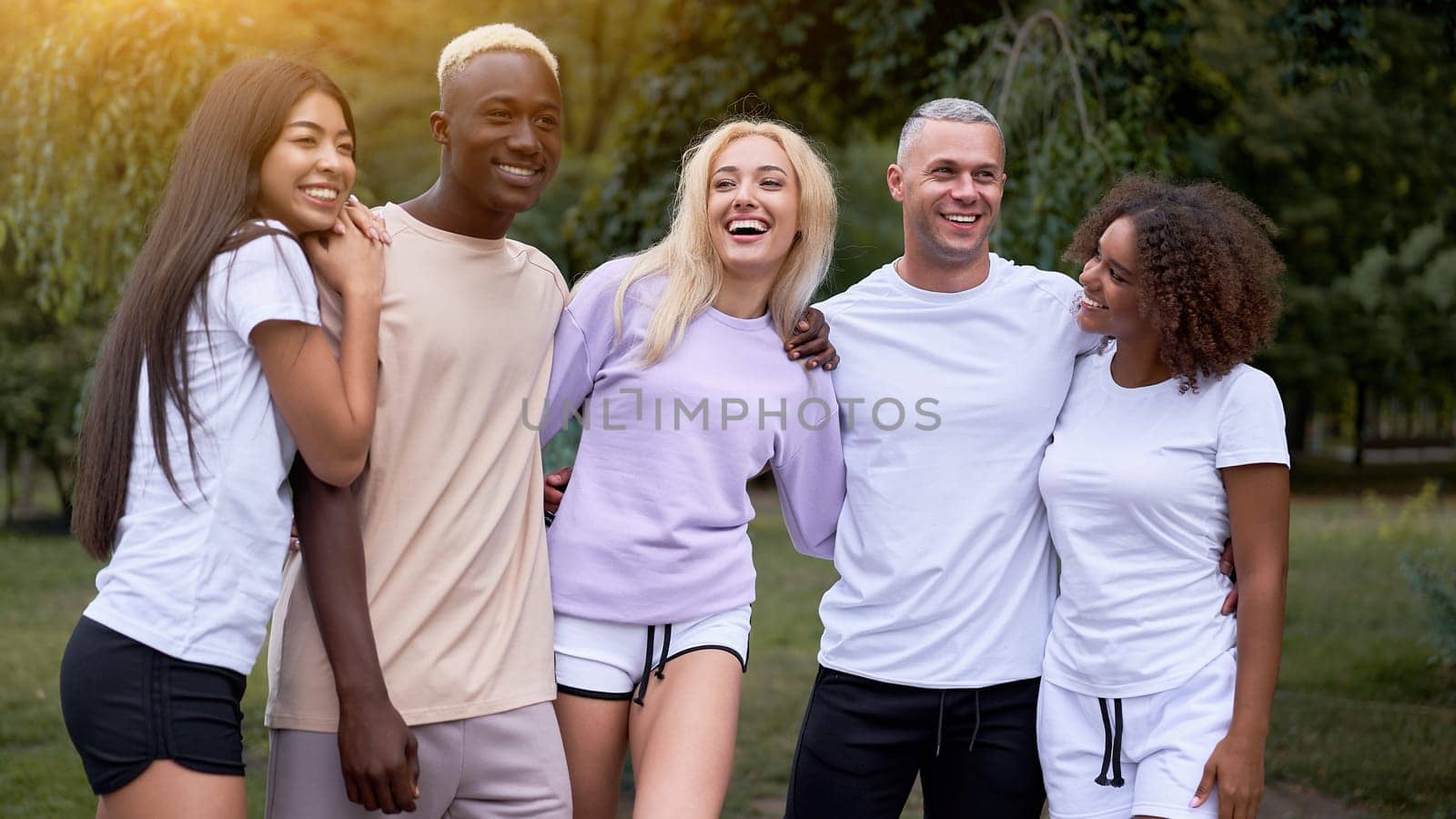 Multi-ethnic group teenage friends. African-American Asian Caucasian students spending time together Multiracial friendship. Happy smiling People in sportswear meeting in park.