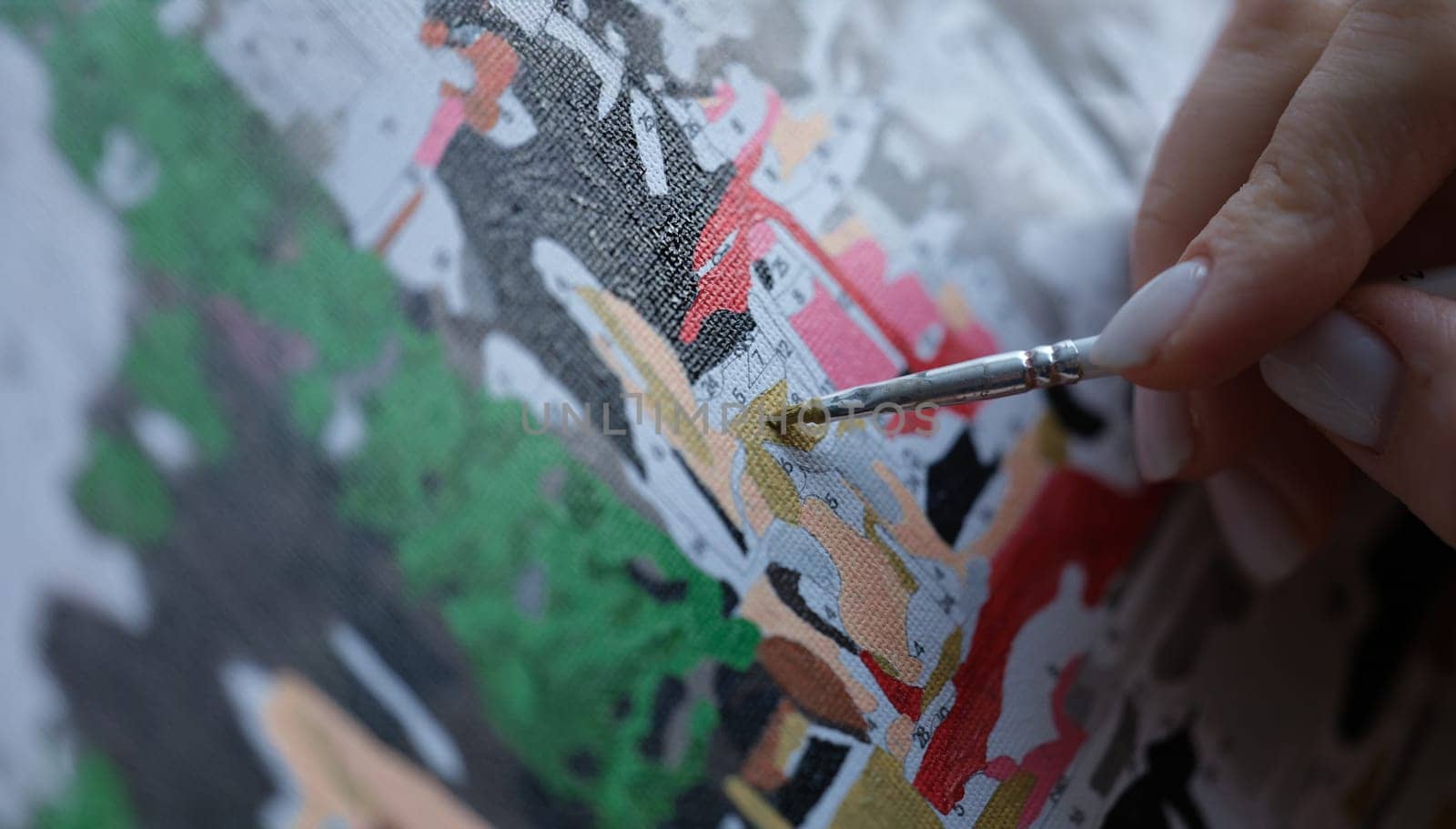 Close-up of woman painting with brush on canvas by numbers. Picture by numbers. Creative hobby or painting for beginners. Leisure activity at home