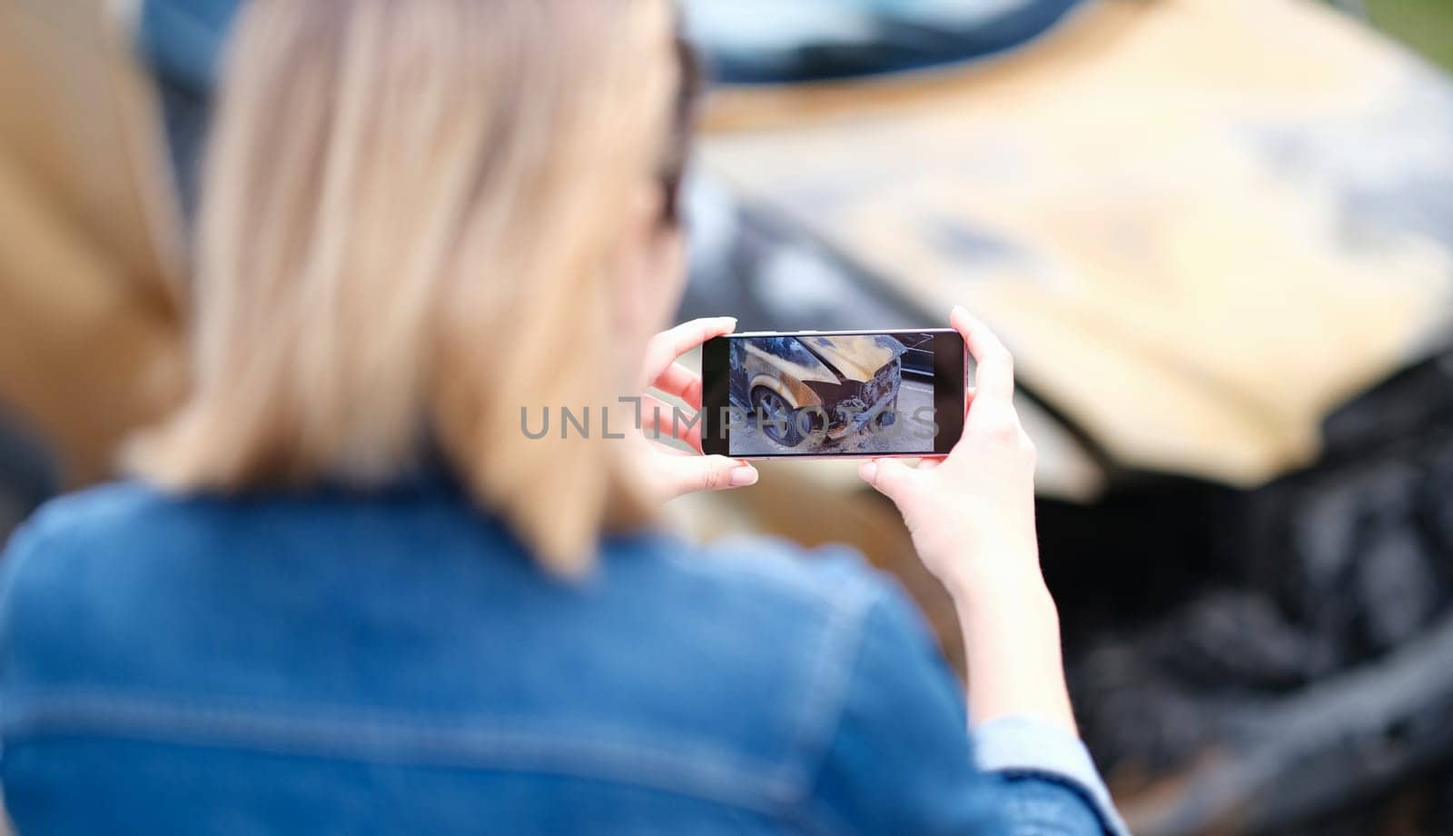 Woman insurance broker making photo of burnt car. Automobile accident and insurance case concept