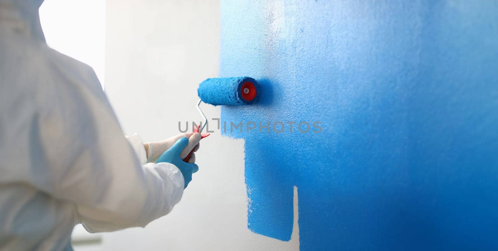 Close-up of painter with brush tool covered in blue colour painting wall. Renovation interior design, construction site and project concept