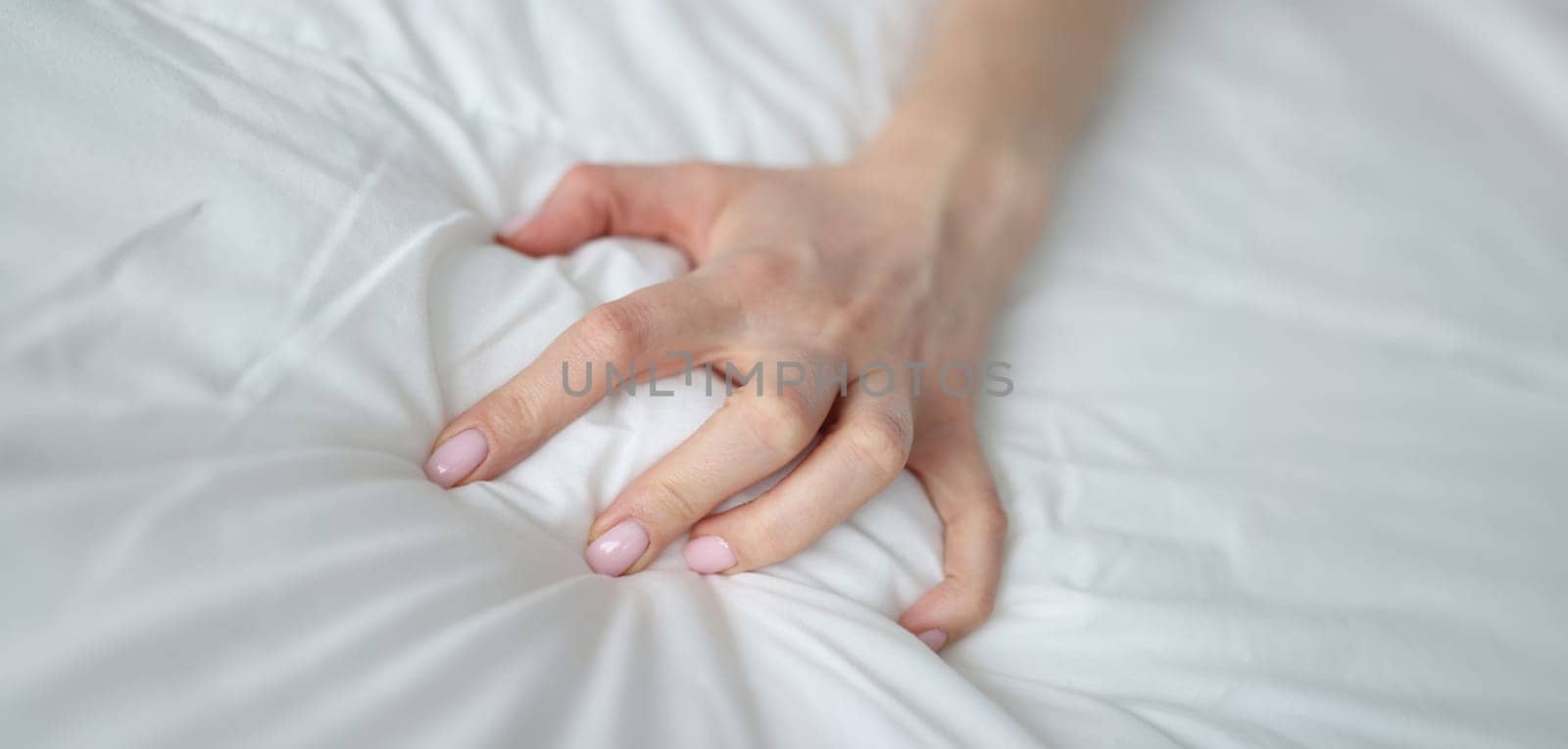 Close-up of sexy female hand pulling and squeezing white sheets in bed. Tender woman hand with sensual manicure. Sexy, pleasure and erotic concept