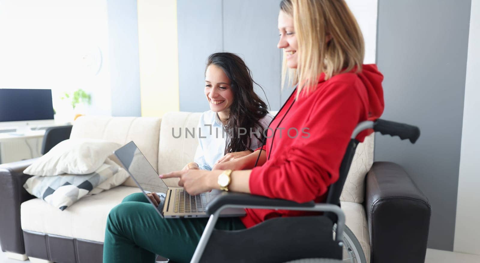 Portrait of smiling friends looking at photos on laptop, woman in wheelchair and disabled people. Pastime together concept