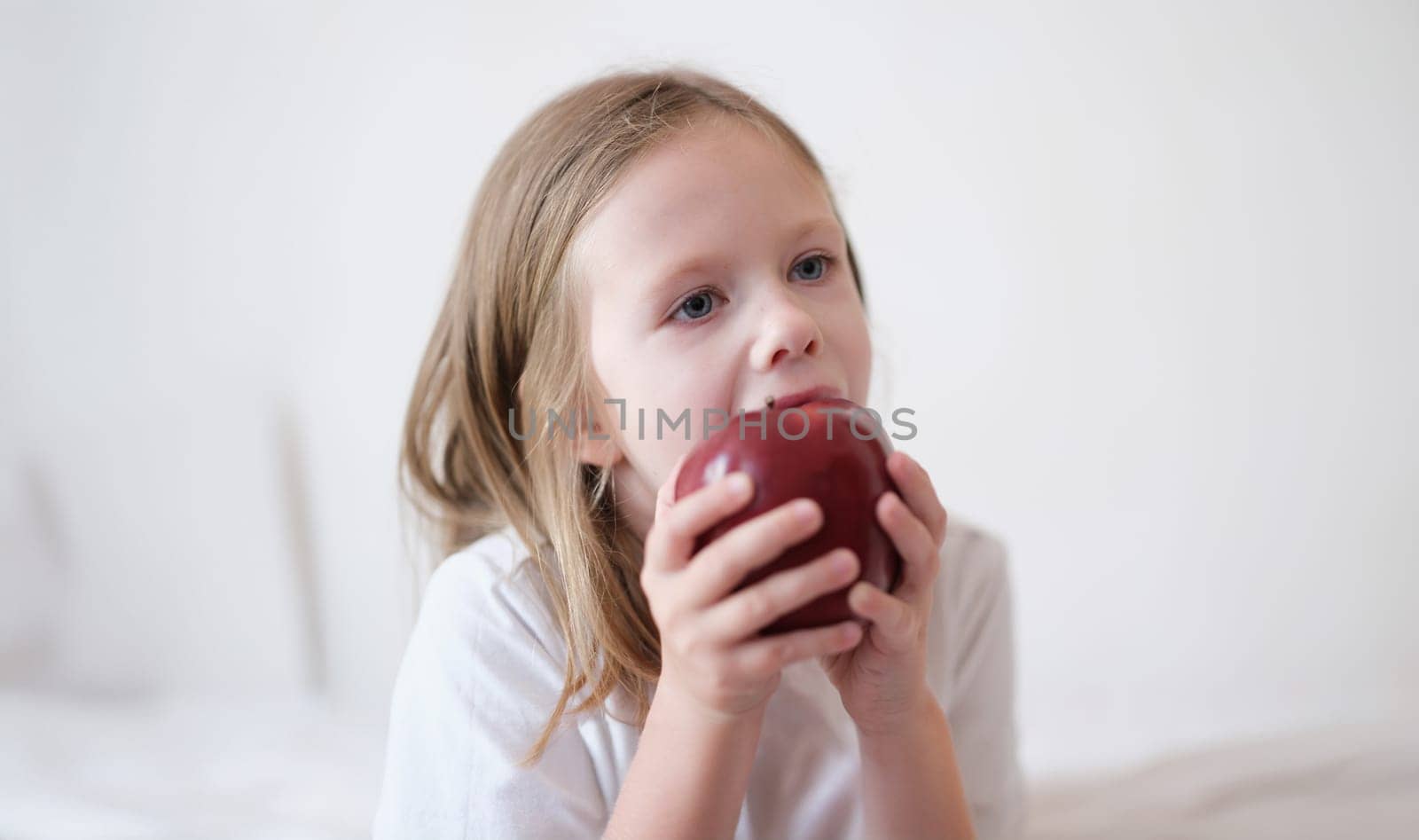 Portrait of little girl eating heartily fresh red apple. Small child holding big apple in hands. Healthy food and vitamins