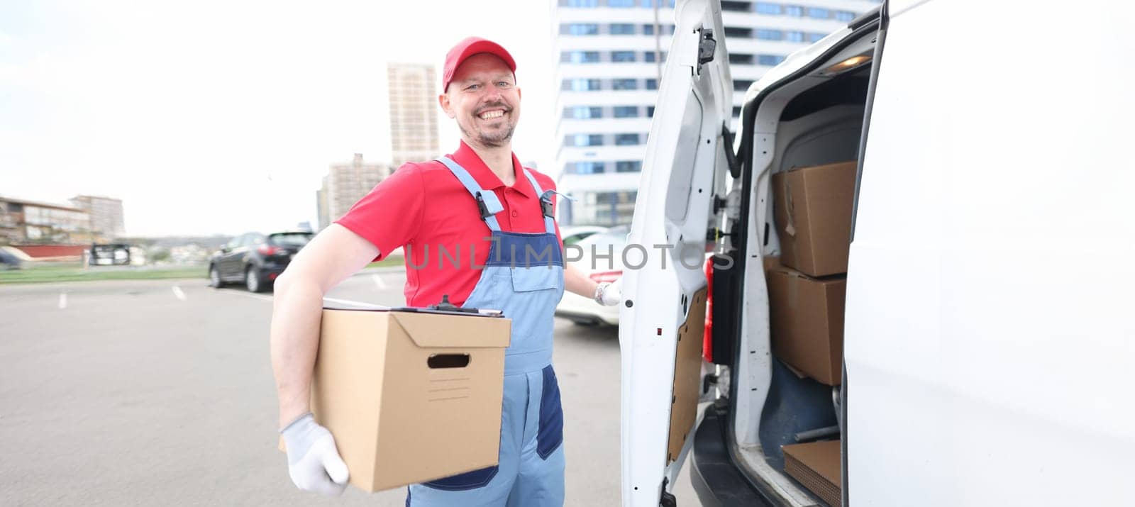 Portrait of smiling courier with parcels near delivery van. Deliveryman holding parcel. Delivery service and receiving packages concept