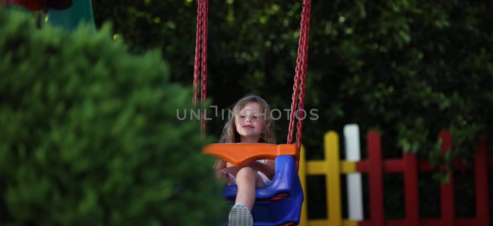 Portrait of little smiling girl riding swing on playground outdoors. Swing ride, cheerful child swinging. Happy kid having fun. Childhood concept