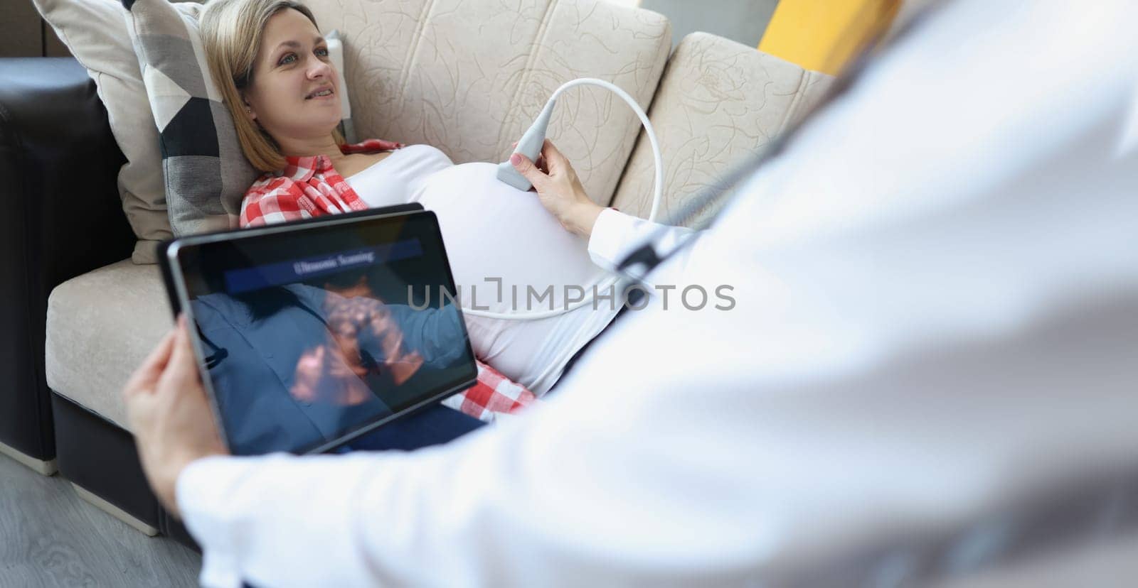 Close-up of gynecologist doing ultrasound scan on belly using modern digital ultrasound machine with tablet. Female patient expecting pregnancy. Gynecology concept