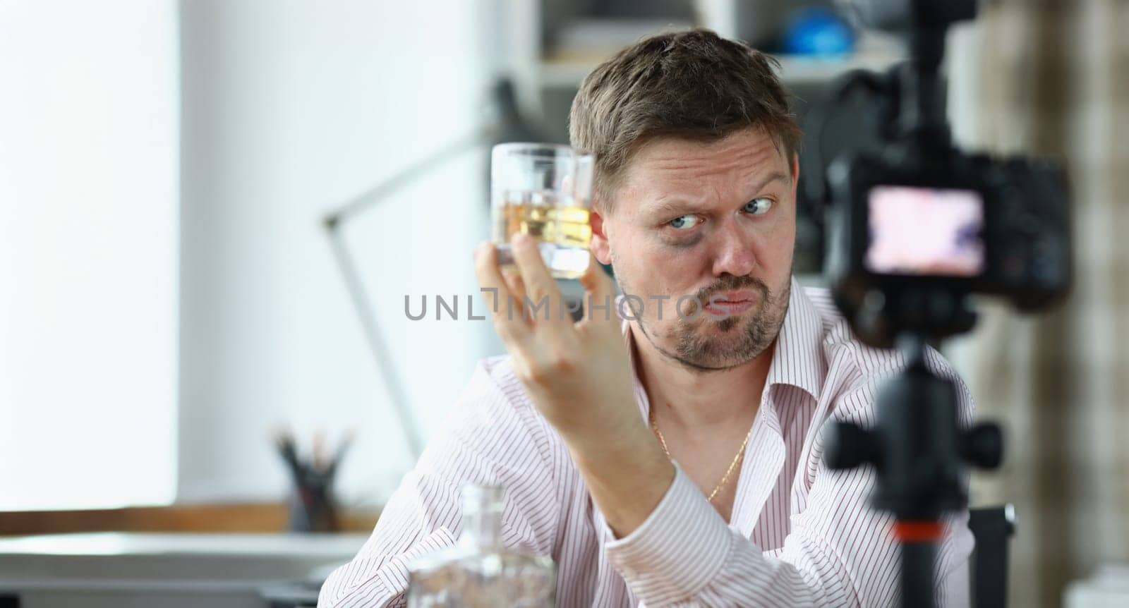 Portrait of video blogger making content for internet channel. Man showing glasses with alcohol drink and looking incredulously. Blogging and vloggonig concept