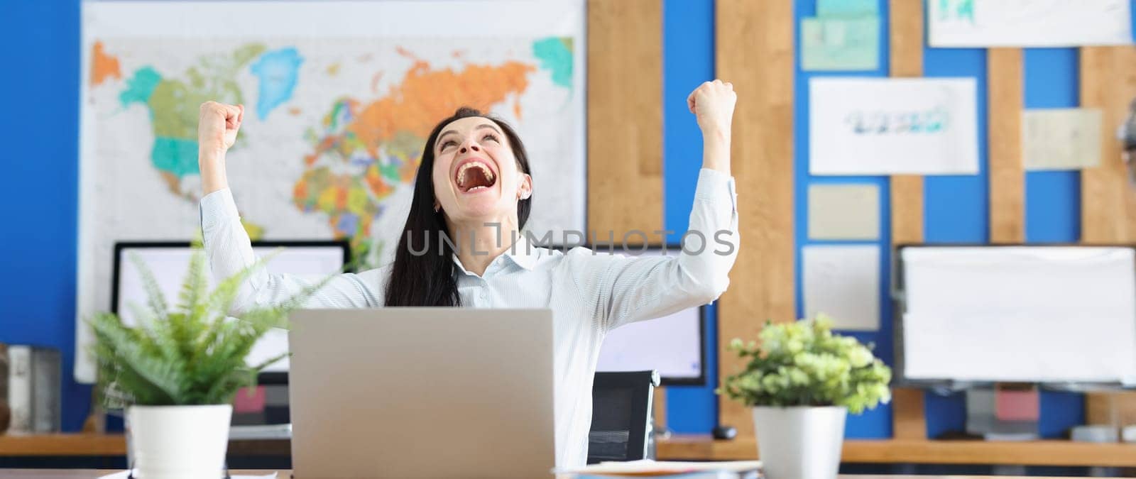Portrait of woman sitting at table in front of computer happy to finish business task, to pass test successfully. Achieve agreement or goal achievement in cooperation