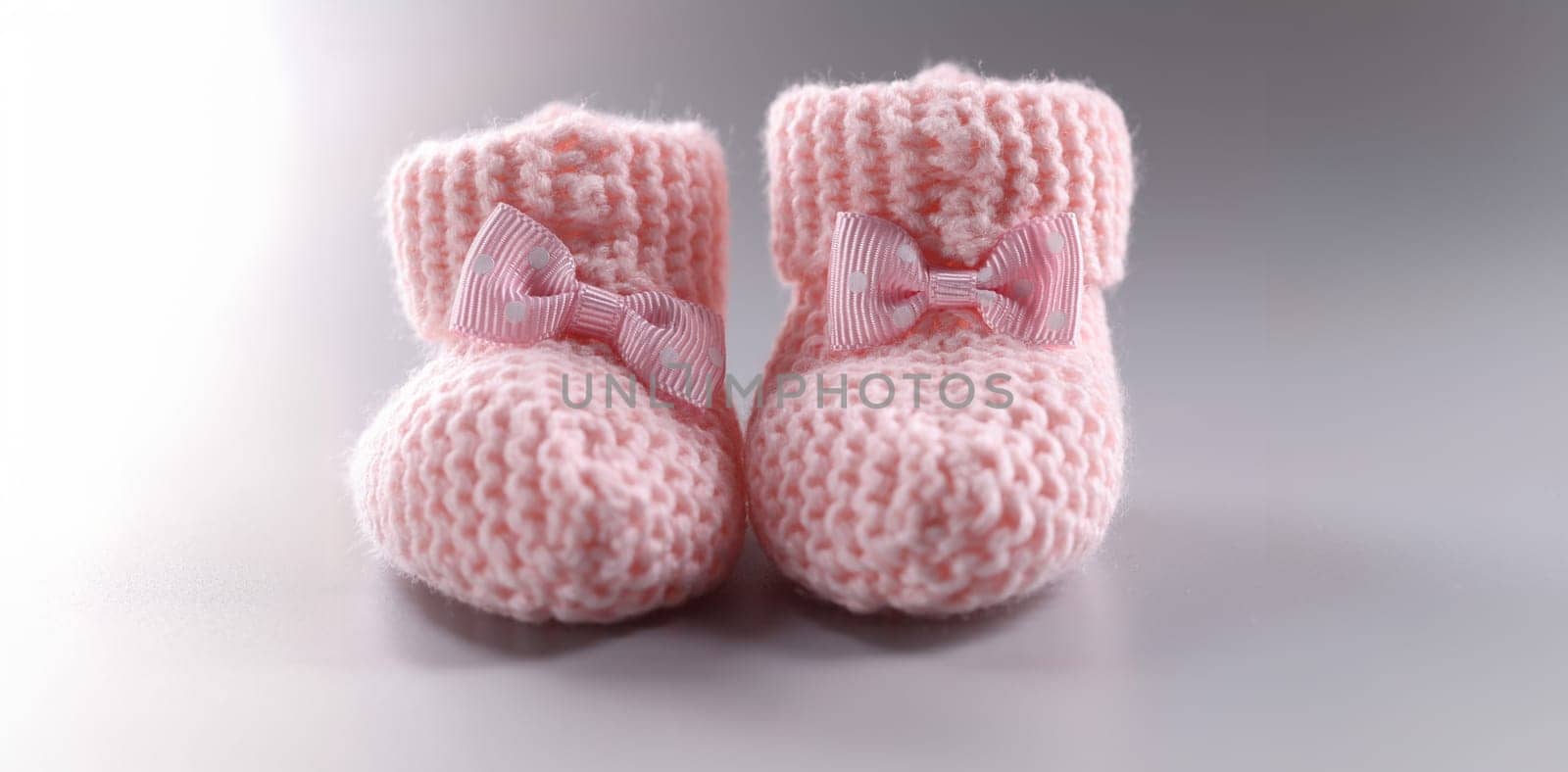 Close-up of handicraft shoes for newborn baby on grey background. Pair of knitted pink baby booties with cute bow. Handmade, preparation for childbirth concept
