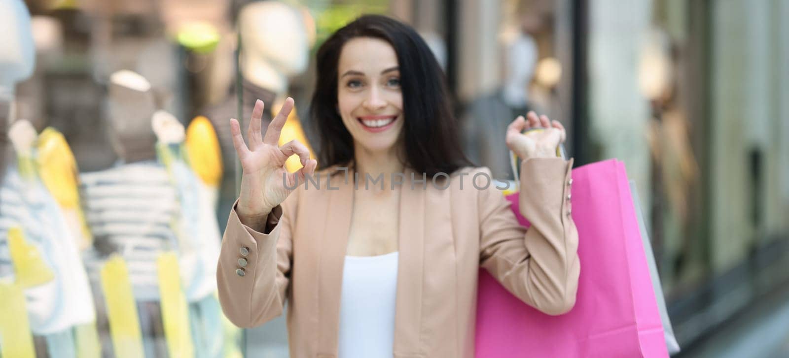 Portrait of happy smiling woman with shopping bags showing ok gesture. Success shopping, purchasing goods and shopaholism concept