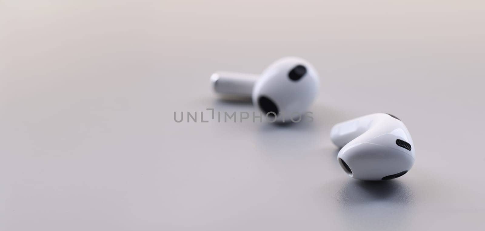 Close-up of new white wireless earphones, on grey background. Listen music or connect everywhere. Trendy technology and gadget device concept