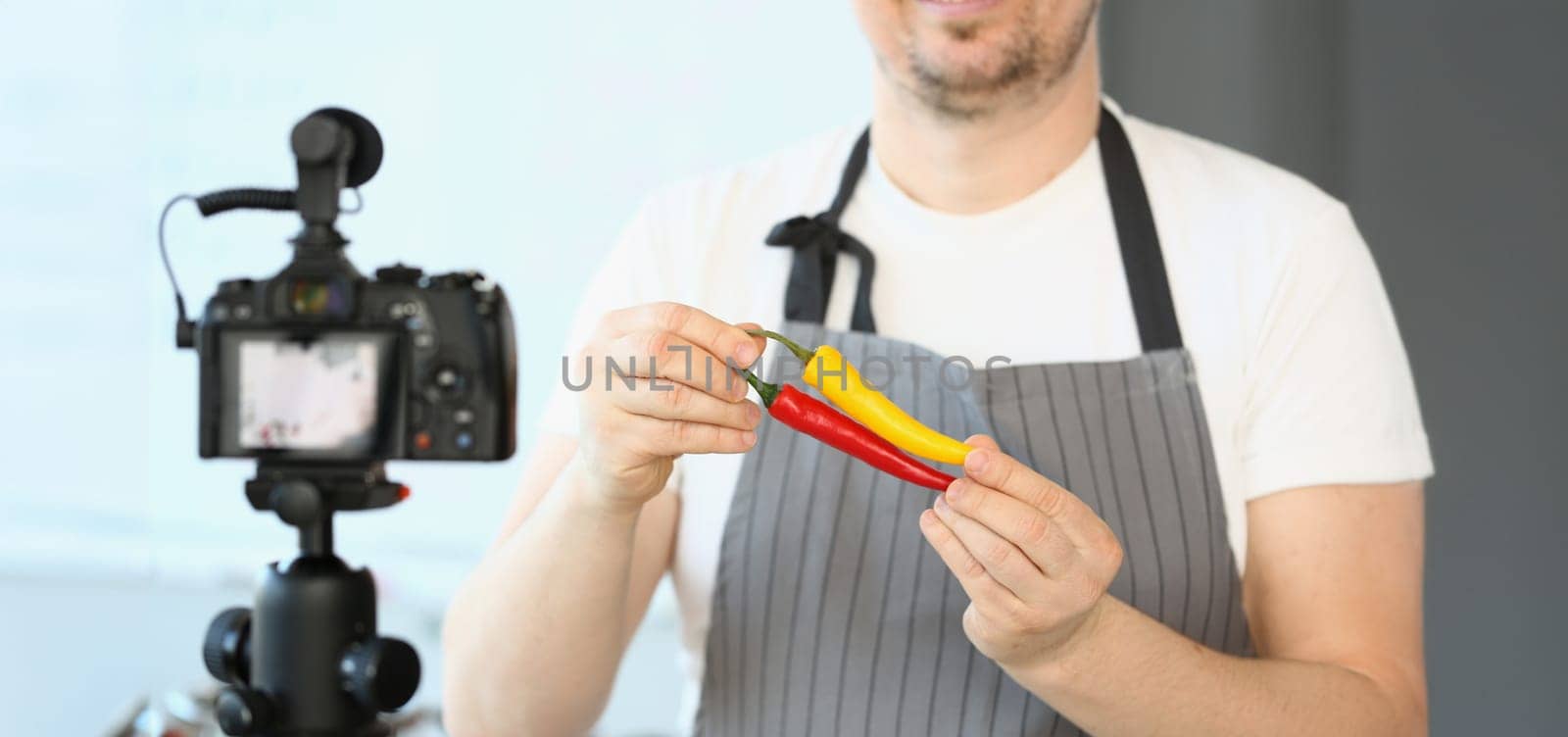 Close-up of male chef in apron showing chilli pepper on camera. Blogger recording video for vlog. Hobby, making content for video vlog concept