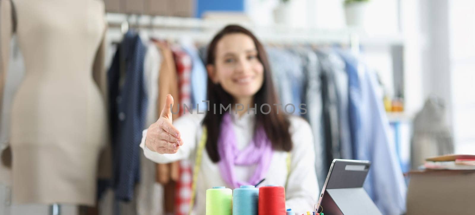 Close-up of woman seamstress giving hand for handshaking, bright sewing accessories on table. Colourful spools of thread. Hobby, art, sewing concept