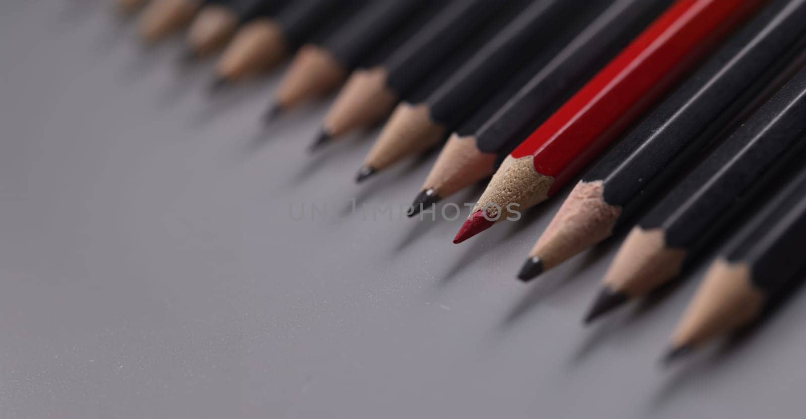 Close-up of one red pencil between row of black pencils. Stand out from crowd, not like everyone else and individuality concept
