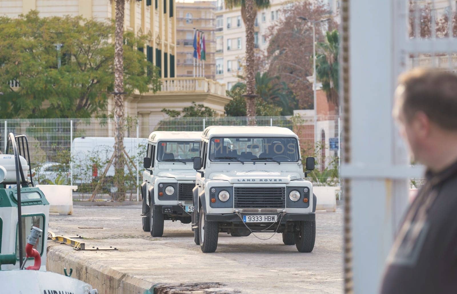 Spain Malaga Land Rover Defenders parked on city quay, with onlooker and flagpole in serene morning or evening light download image