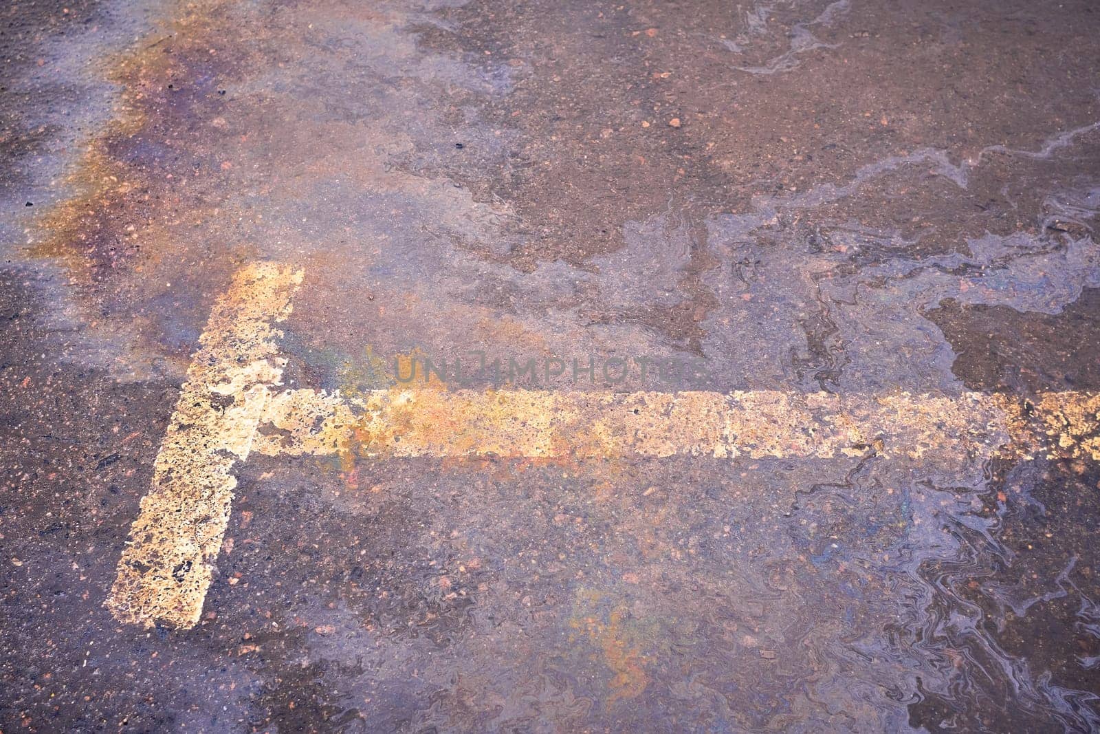 Oil spill on wet asphalt, parking lot with dividing line.