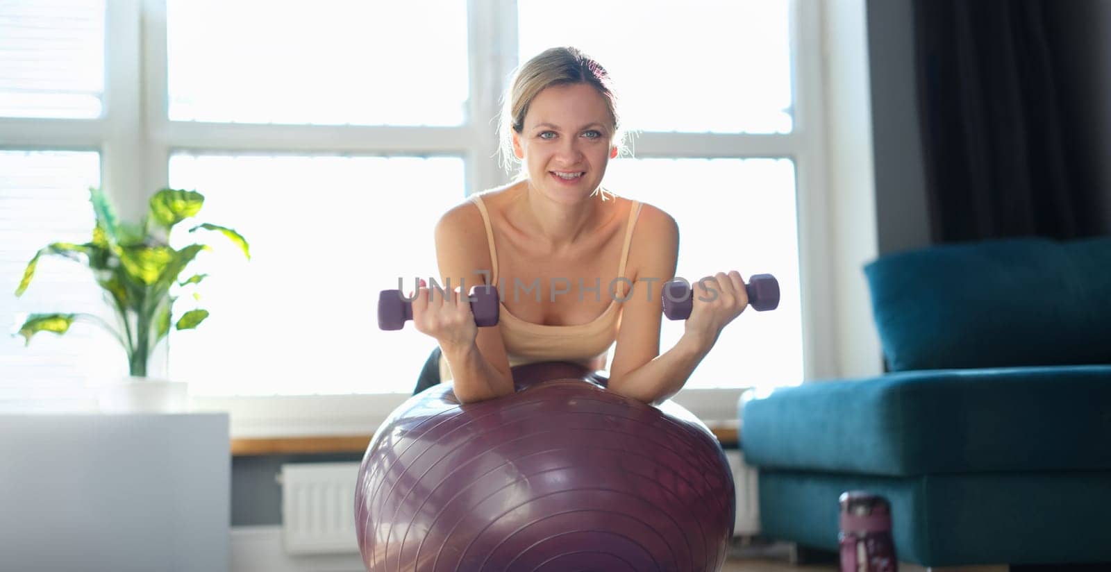 Portrait of smiling woman doing exercise with dumbbells on fitness ball. Fitness equipment for sport activity. Healthy lifestyle concept