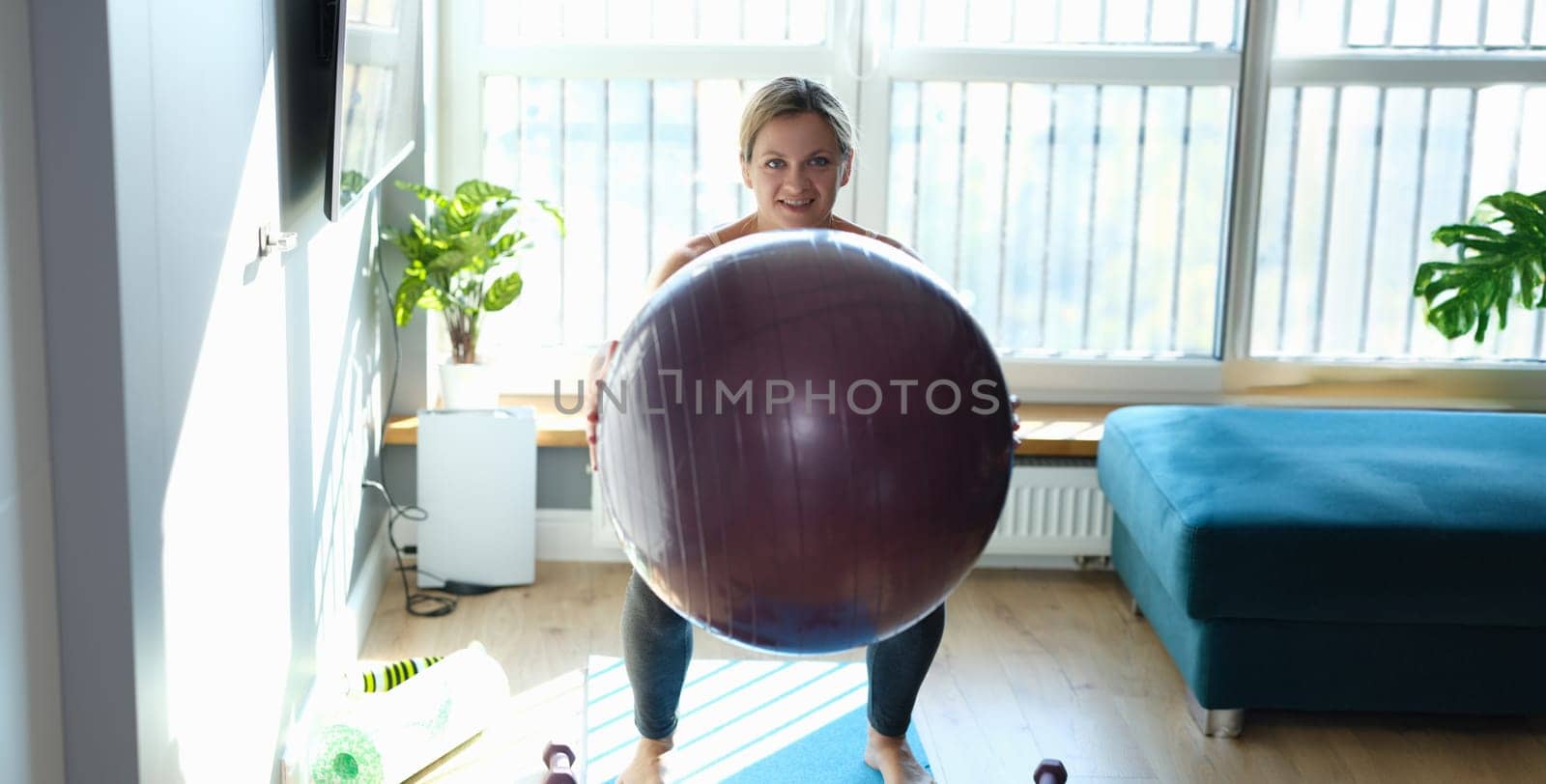 Portrait of sporty smiling woman doing exercises with fitness ball at home. Healthy lifestyle and fitness equipment for sport activity concept