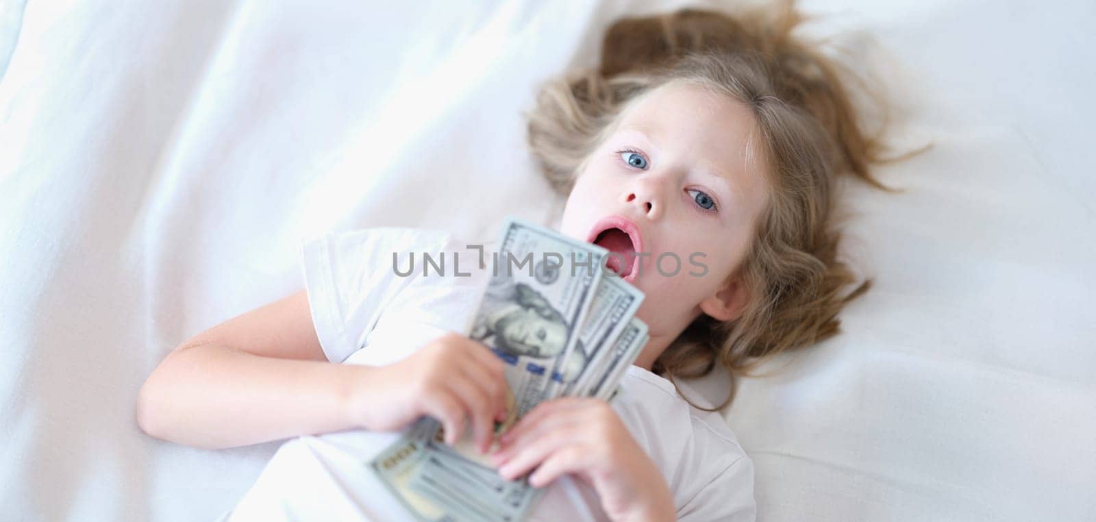 Portrait of small cheerful girl holding cash in hands. Little smiling child counting money, happy childhood.