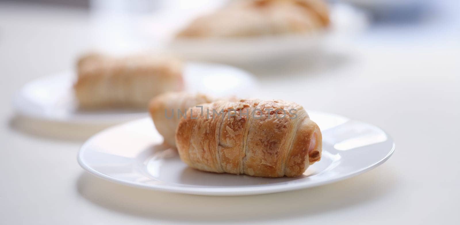 Close-up of homemade sausages in dough on white plate. Freshly baked sausage rolls. Lunch and yummy snack concept
