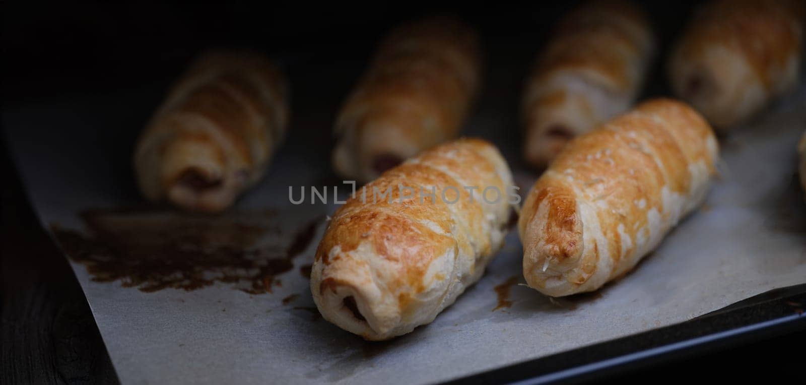 Close-up of homemade sausages in dough on baking sheet. Freshly baked sausage rolls. Lunch and yummy snack concept