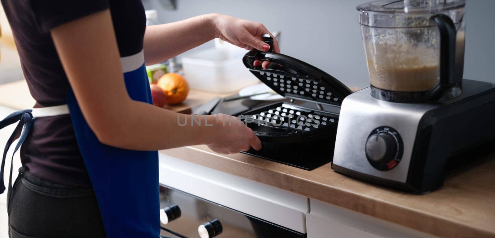 Close-up of woman preparing belgian waffle maker in kitchen. Waffle iron in kitchen. Preparing homemade waffles