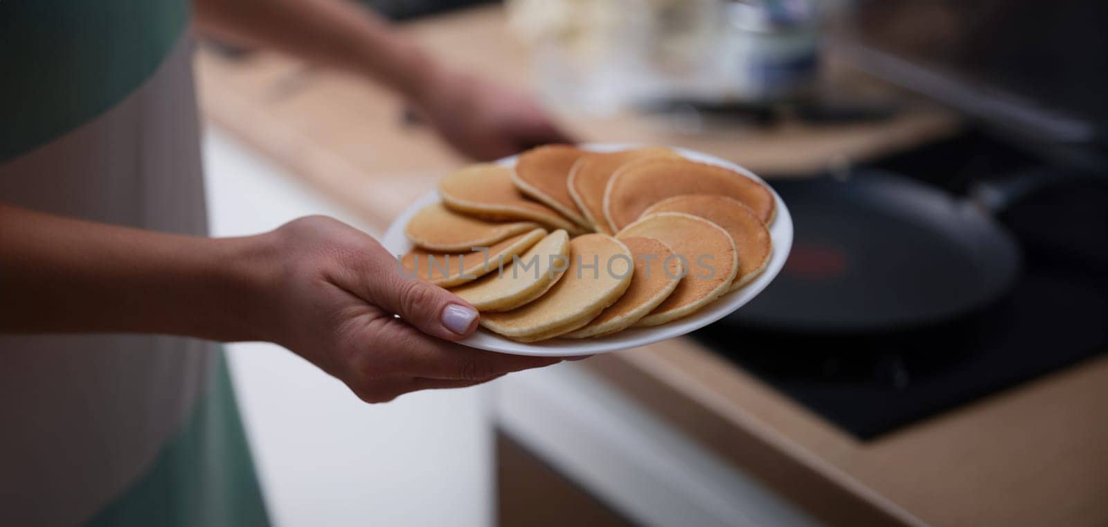 Close-up of female hands holding plate with tasty fresh homemade pancakes. Hot delicious meal for breakfast, nutritious food to start day. Food, eating concept