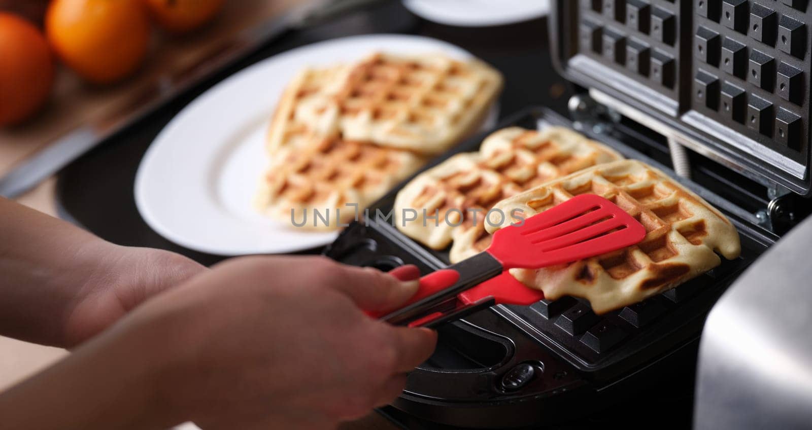 Close-up of waffle iron in kitchen, cooking homemade waffles. Woman preparing yummy breakfast for family