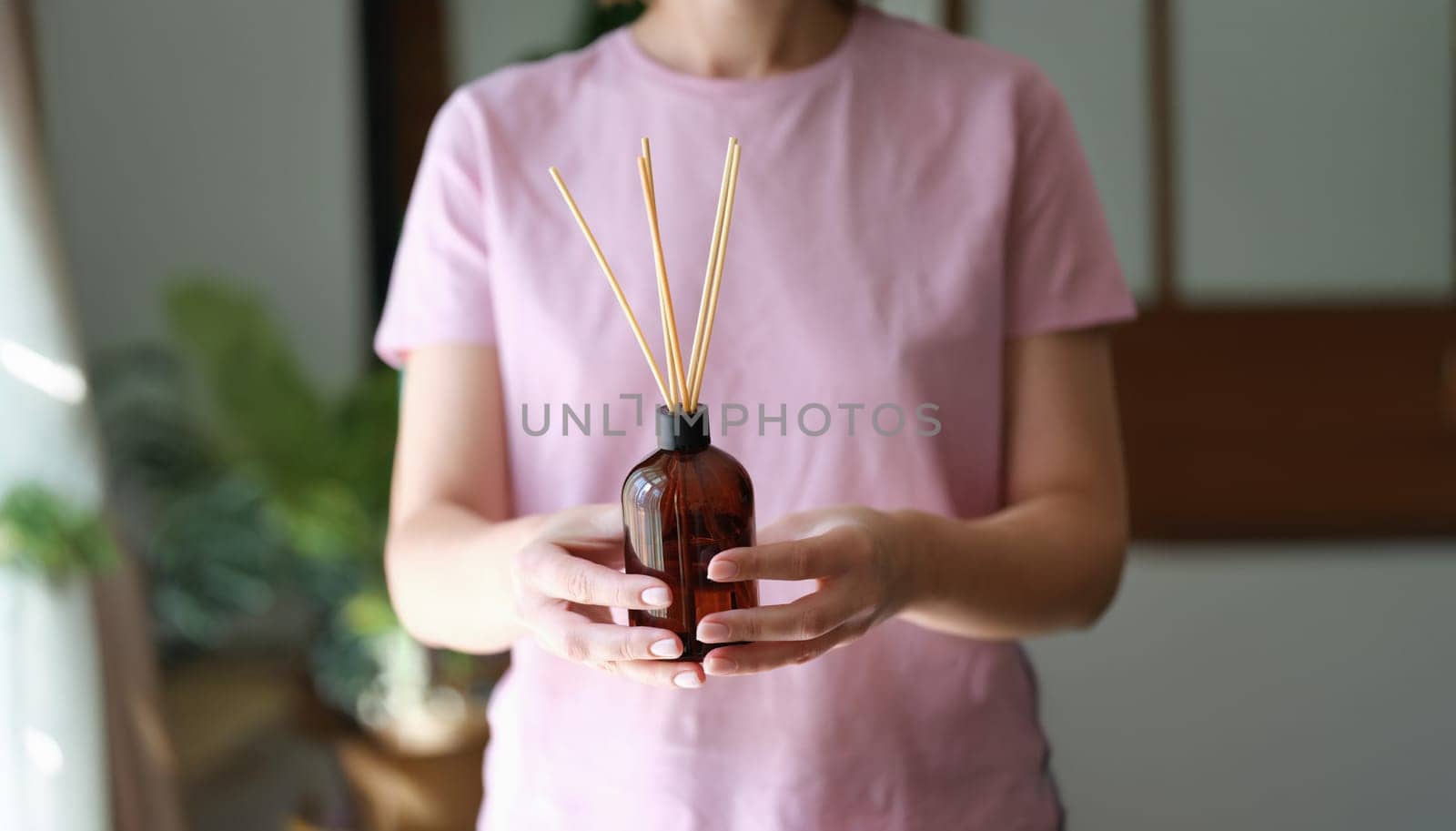 Close-up of woman holding aroma reed diffuser, home fragrance bottle with rattan sticks and smell of freshness
