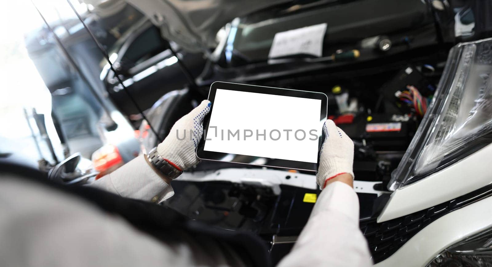 Close-up of mechanic worker using tablet for diagnostics of technical condition of vehicle. Handyman applying digital tablet at car service. Maintenance concept