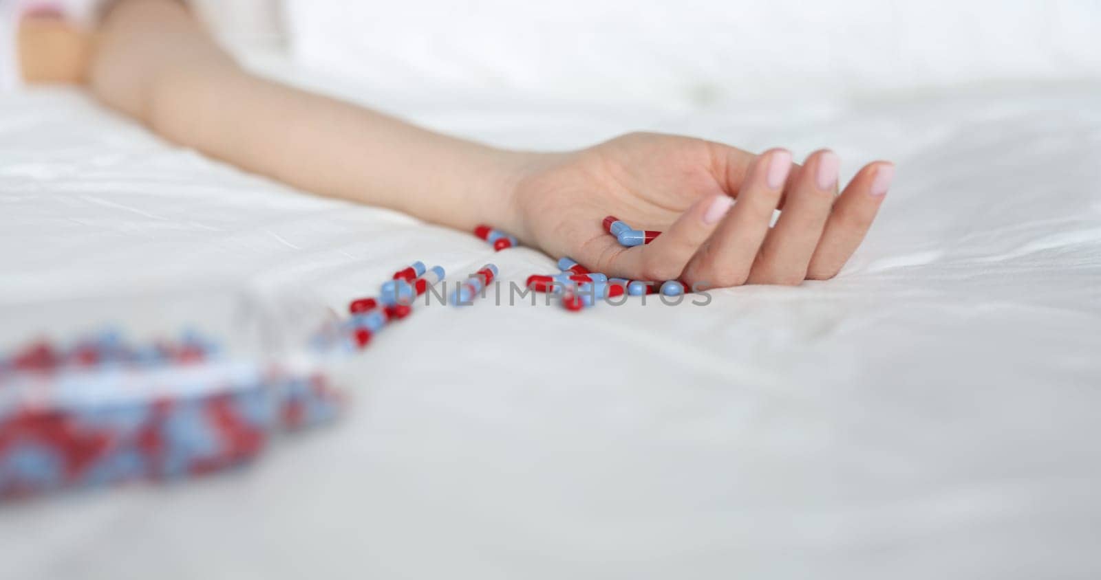 Close-up of young woman committing suicide by overdosing on medication. Overdose pills and addict. Female lying on bed and scattered pills on bedclothes