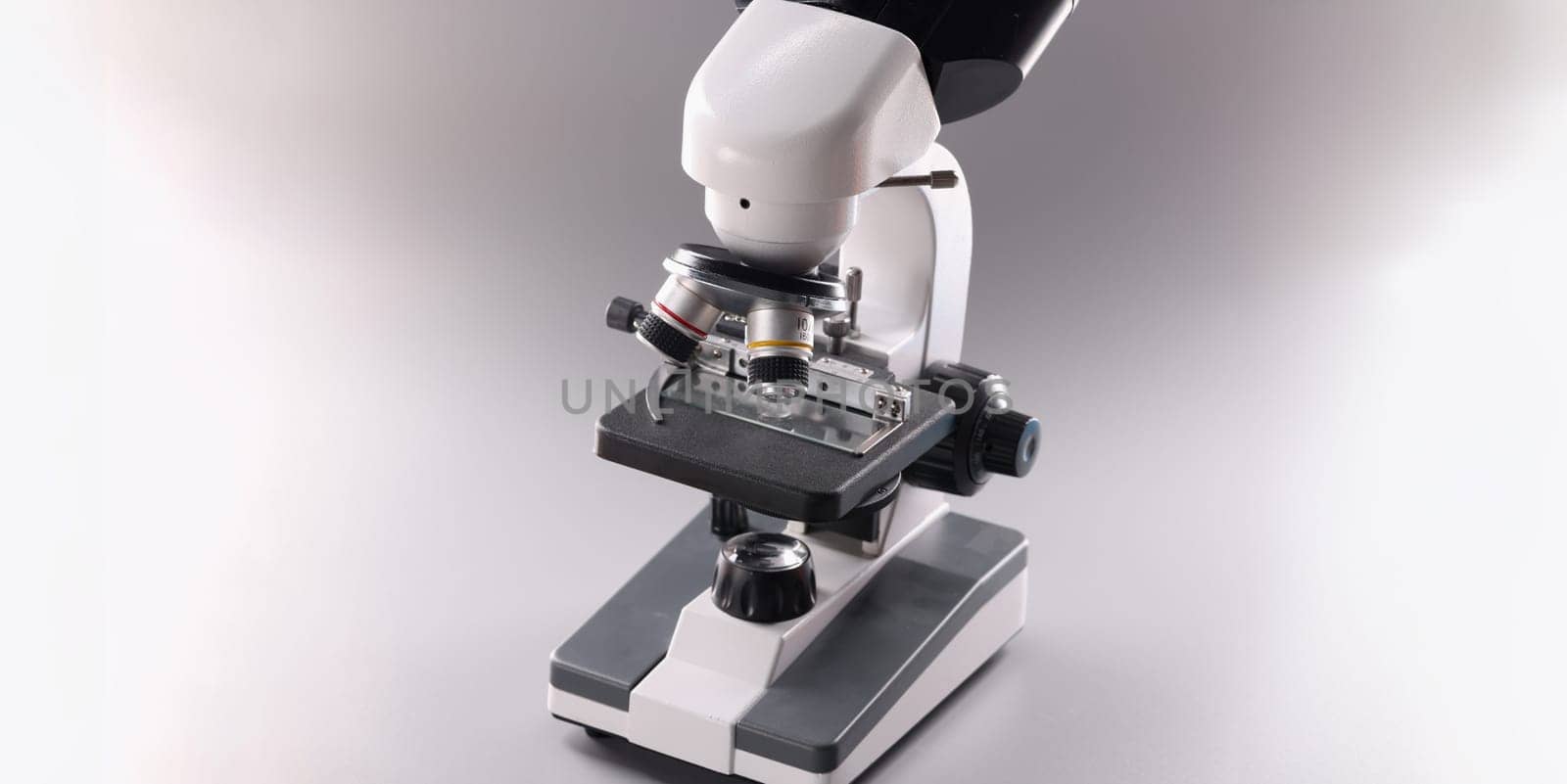 Close-up of modern microscope tool for laboratory research on grey background, magnifying device for precise results of research or experiment. Scientific appliance