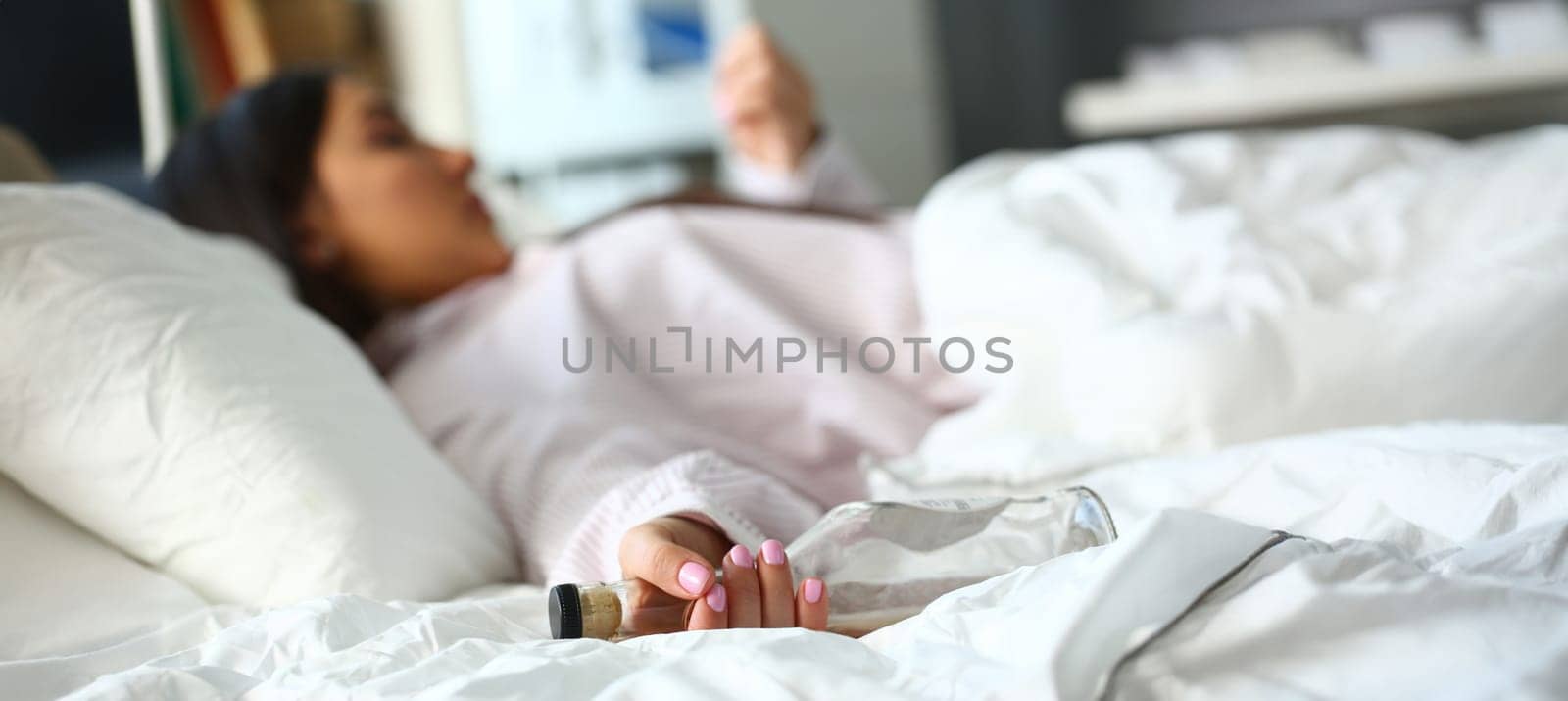 Close-up of drunk woman sleeping in bed and holding empty bottle. Person suffering from alcoholism. Female alcoholic and overdose or alcohol abuse concept