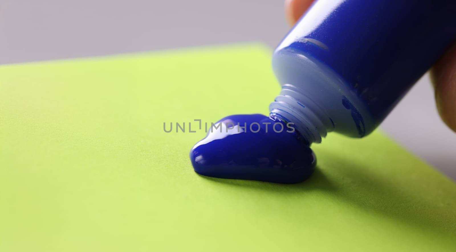 Close-up of tool for further creative masterpiece, paints for drawing . Artist squeeze paint out of tube, bright blue colour on green paper. Art and creativity hobby concept