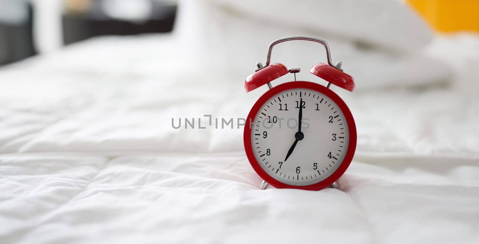 Close-up of red alarm clock at 7 oclock on bed. Early morning, daily regime and working day. Lack of sleep idea. Alarm-clock morning wake-up time concept