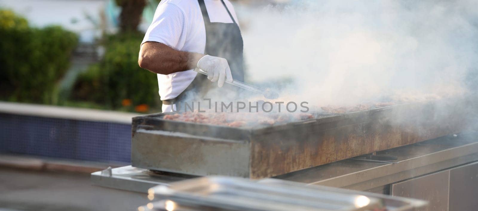 Close-up of chef cooking barbecue meat outdoors, summer lifestyle. Man grilling meat dish. Summer food festival, bbq event cooking