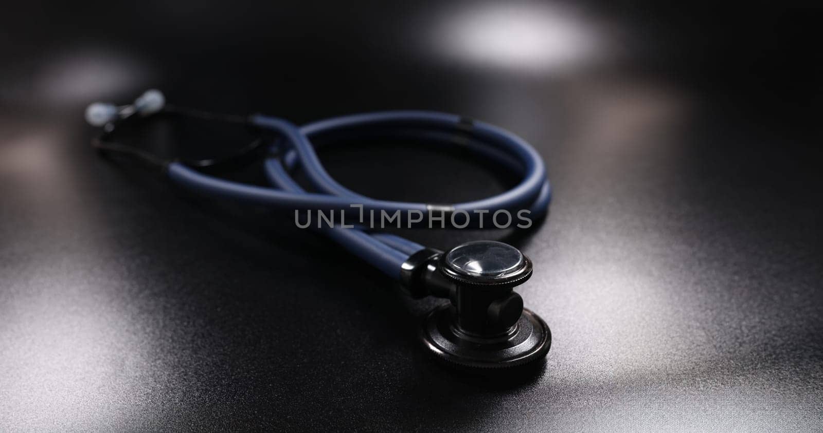 Close-up of dark blue medical stethoscope on black surface. Medical instrument for listening to action of heart or breathing. Medicine and healthcare concept