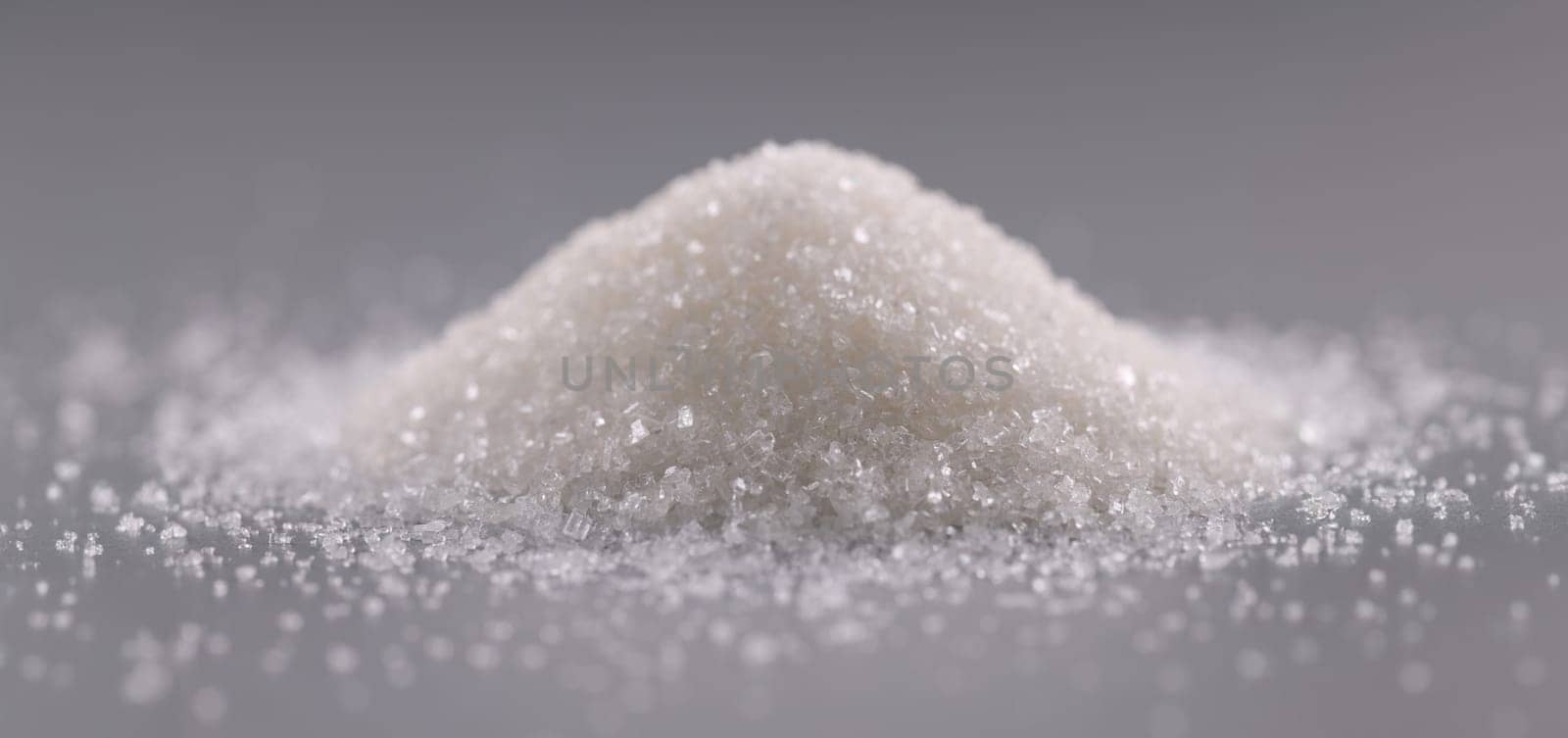 Close-up of pile of sugar crystals on grey surface, heap of sweet powder to add in dishes. Ingredient for cooking food, sweet crystalline substance concept
