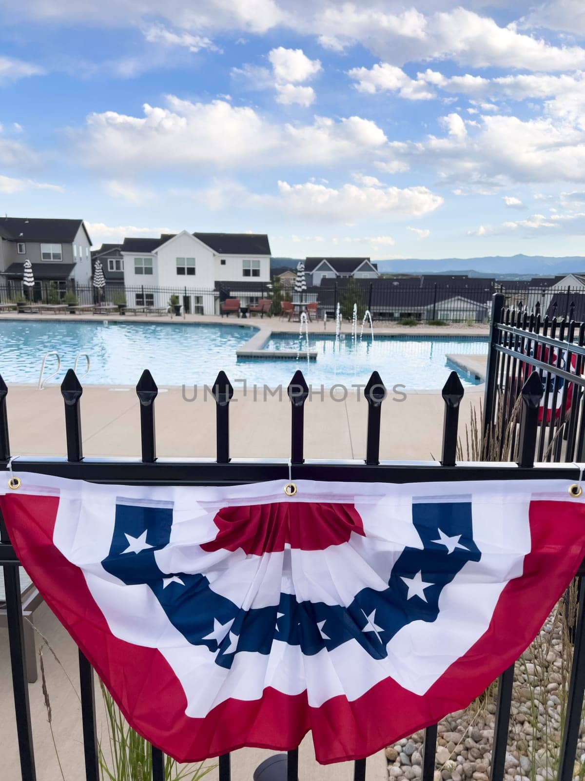 Castle Rock, Colorado, USA-July 6, 2024-A neighborhood pool area decorated with a red, white, and blue bunting flag hanging on a black iron fence. Houses and loungers are visible in the background, creating a festive and inviting atmosphere.