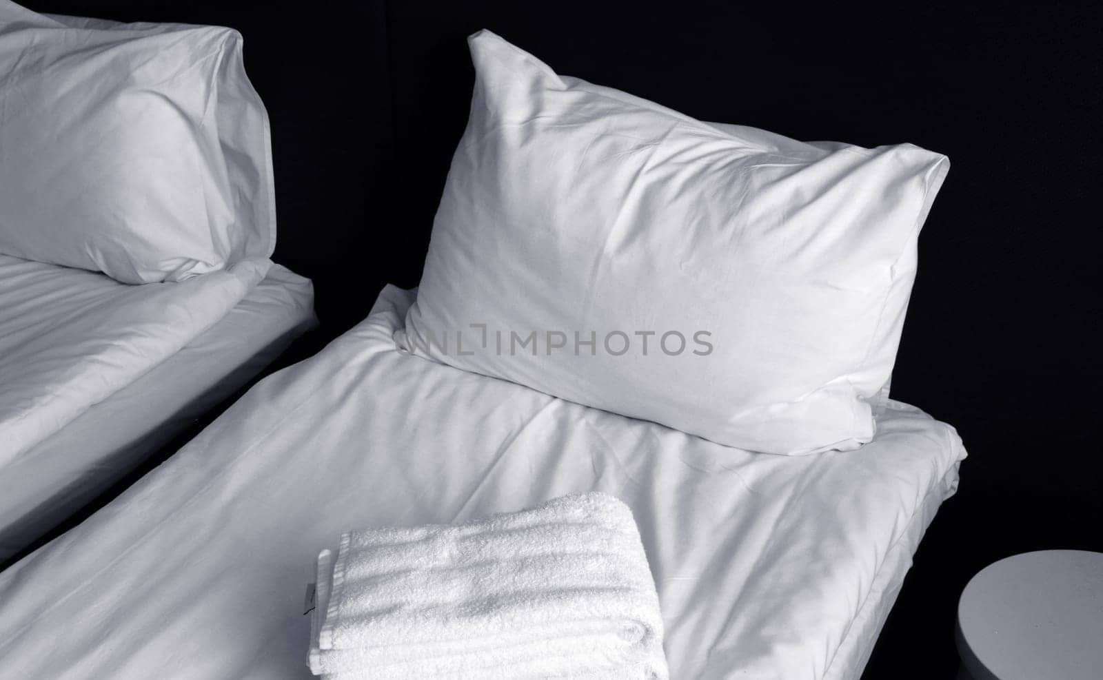 The bed is covered with a fresh white sheet, a white pillow, and a laying towel. Fragment of a cozy bedroom.