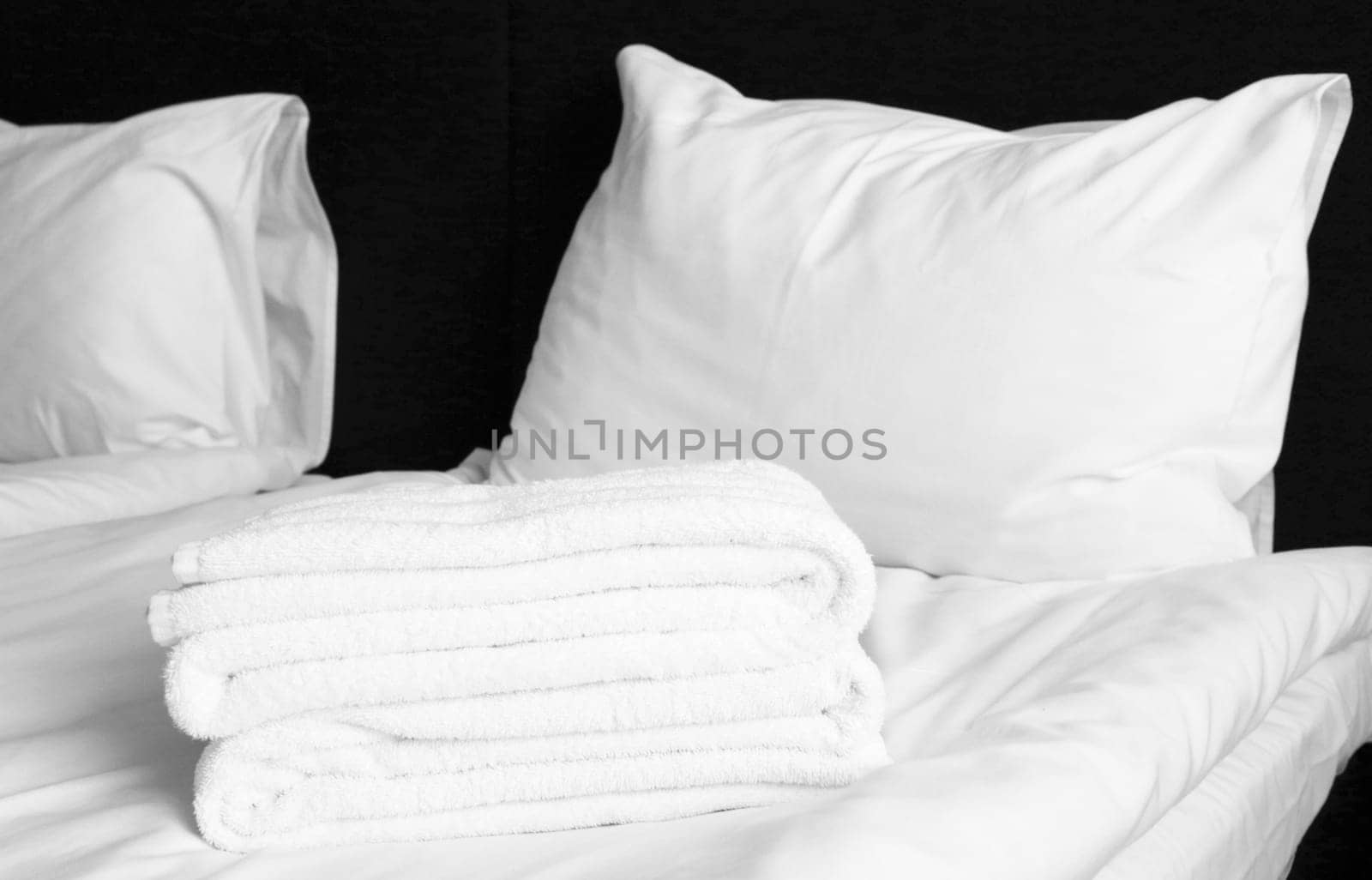 Two pillows, folded terry white towels on a sheet on a black background.