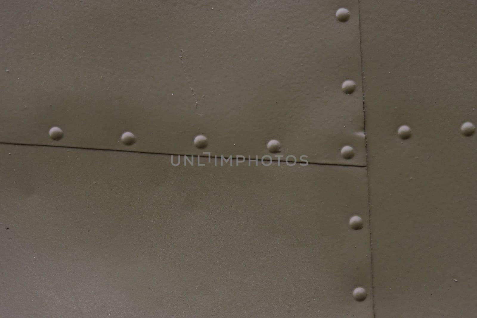 The surface of a metal wall with green rivets. Airplane fuselage painted green.