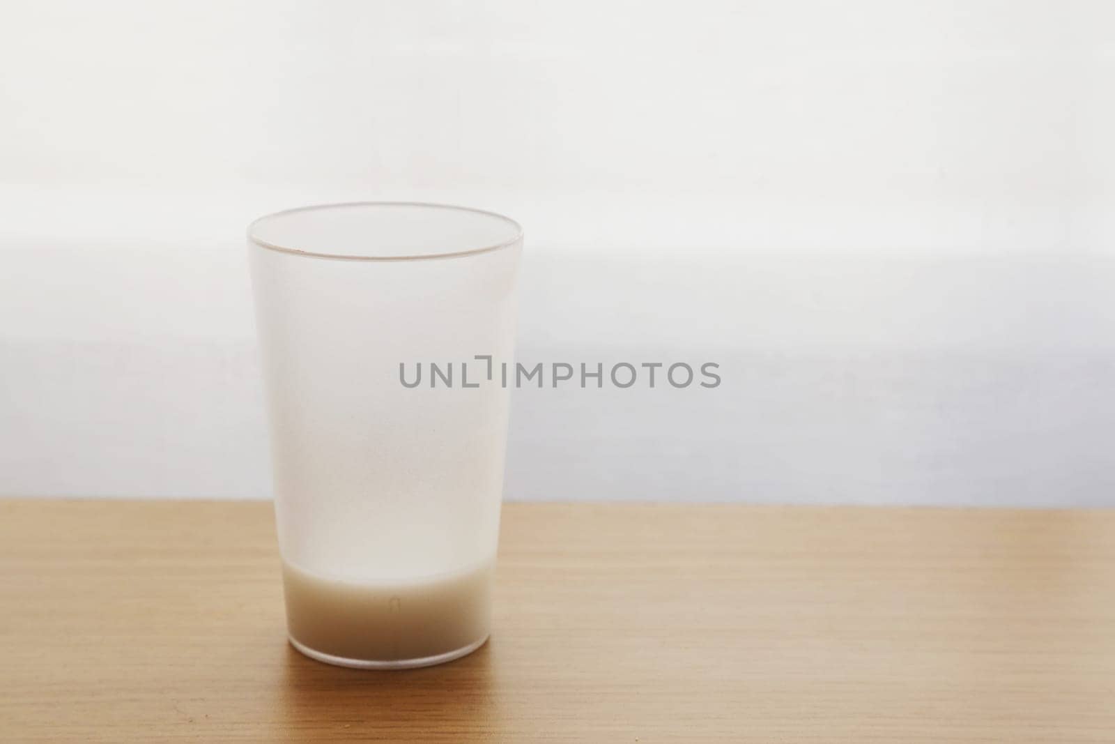 A half-full glass of drink stands on a brown table opposite the window.